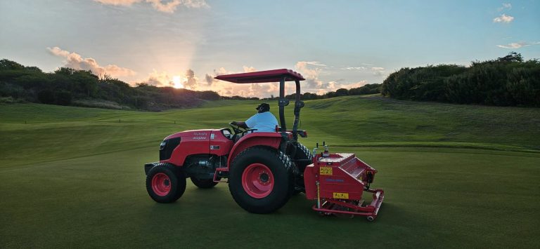 Groundskeeper on red tractor maintaining the green at sunrise at Old Quarry Golf Course Curaçao