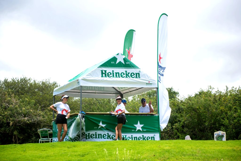Heineken-branded tent with staff and flags at Hole 15 during golf tournament in Curaçao