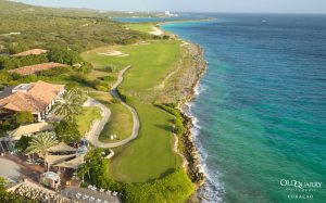 Aerial view of Hole 1 at Old Quarry Golf Course with turquoise sea on the right and a winding fairway protected by (smiley) bunkers.