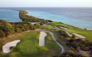 Aerial view of Hole 3, a par 3 at Old Quarry Golf Course, featuring an elevated tee, a green perched behind rocky terrain, and the Caribbean Sea in the background.