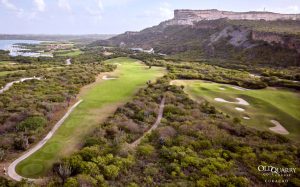 A panoramic view of Hole 5 at Old Quarry Golf Course in Curaçao, showcasing a long fairway framed by native vegetation and dramatic limestone cliffs.