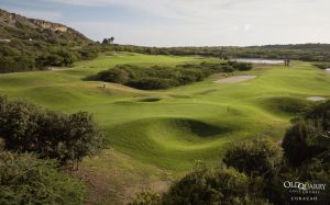 A lush view of Hole 6 at Old Quarry Golf Course with a green guarded by natural ridges, surrounded by rolling fairways, bunkers, and distant water near the marina.