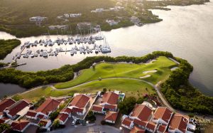 An overhead view of Hole 7 at Old Quarry Golf Course, nestled beside a marina filled with yachts and framed by luxury villas and lush mangroves.