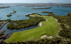 A dramatic aerial view of Hole 8 at Old Quarry Golf Course, showcasing the sharp dogleg left shape wrapping around sparkling blue water and mangroves.