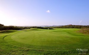 Sunset view across the green of Hole 11 at Old Quarry Golf Course Curaçao, with rolling hills and Landhuis Santa Barbara in the distance.