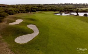 Aerial view of Hole 14 at Old Quarry Golf Course Curaçao, featuring shaped bunkers along the fairway and a water hazard near the green.