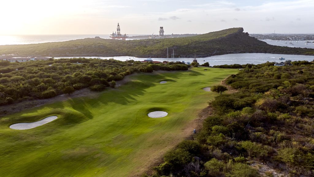 Aerial view of Hole 18 with bunkers, Caribbean Sea, and industrial backdrop at Old Quarry Golf Course Curaçao